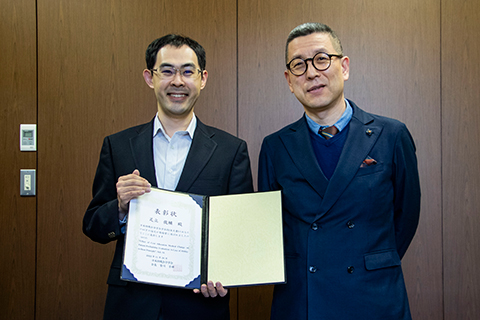 向韓校長(照片右邊)微笑著報告獲獎的足立老師(照片左邊)